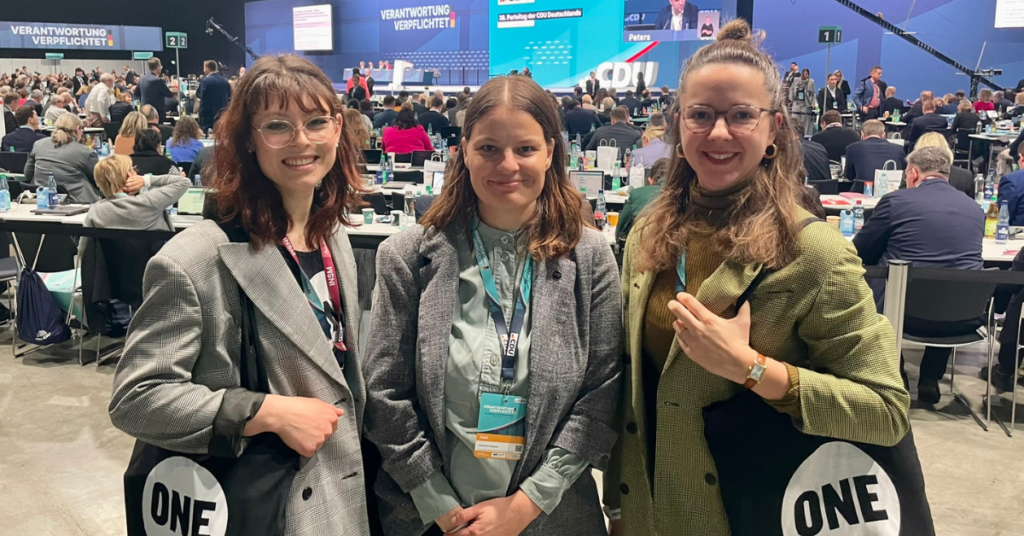 Pia Schwaiger, Lisa Ditlmann und Joanna Klever von ONE Deutschland auf dem CDU Parteitag 2026, im Hintergrund die Delegierten an Tischen und die Bühne.
